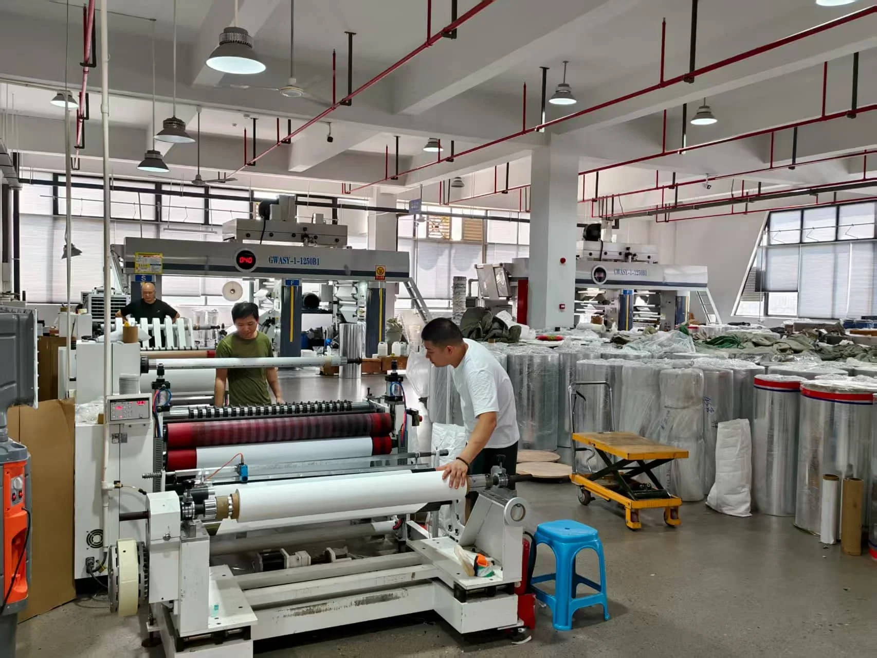 Team members operating a fabric coating machine beside material rolls